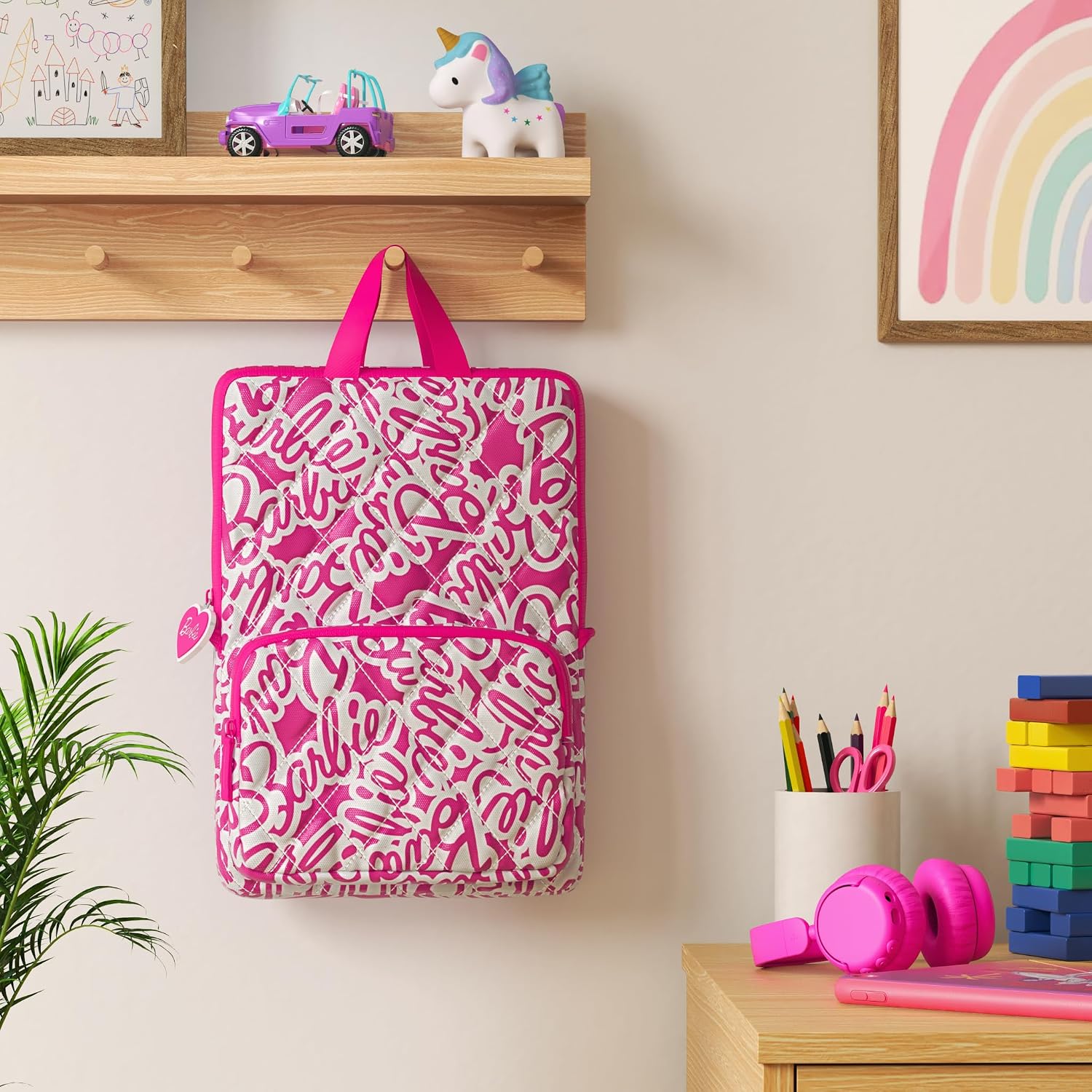 A pink patterned tablet carrying case hanging from a wall peg above a pencil cup and colorful toy blocks